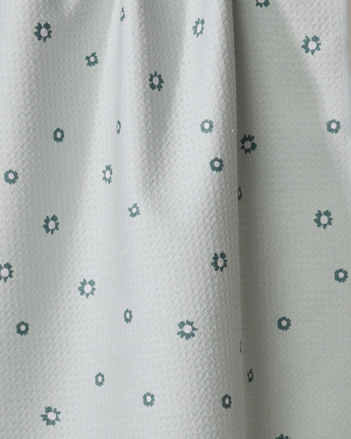 The Forest Daisy by Coit Creative is a light gray towel with small dark green and white flower patterns. Ultra-absorbent and made from recycled materials, it hangs in gentle folds—ideal as a kitchen or tea towel.