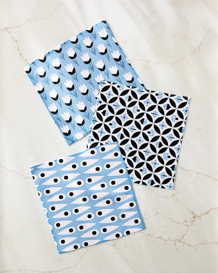 The Anette Heiberg Forest Findings dishcloth set features three blue and white super-absorbent towels with tulip, geometric circle, and striped dot patterns, beautifully displayed on a light marble surface.
