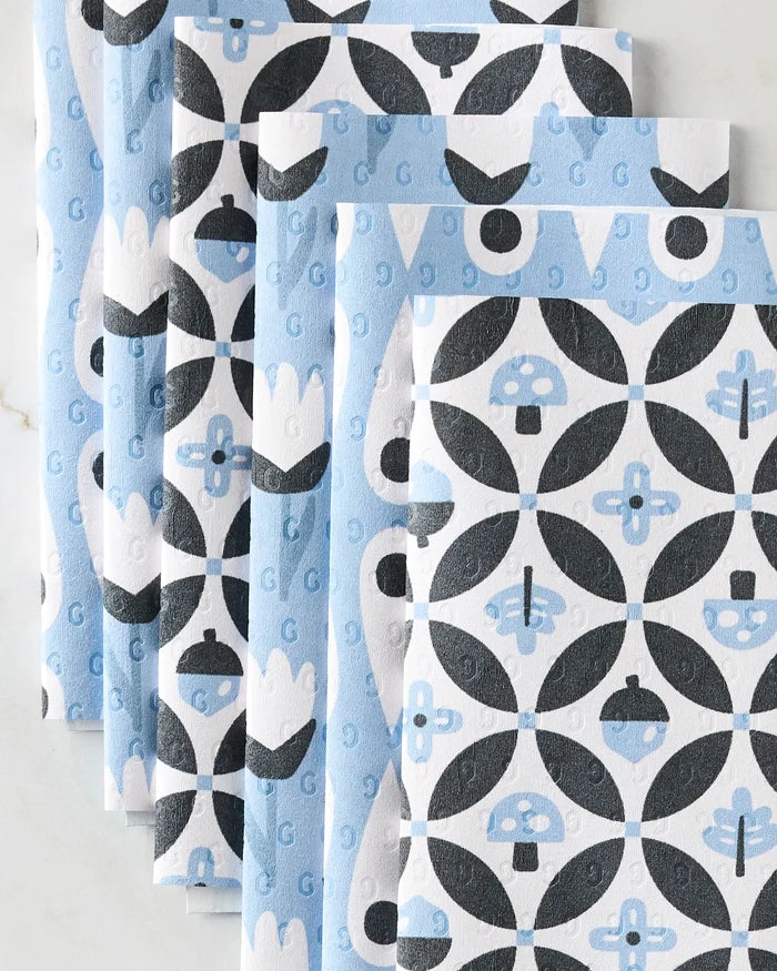 Five folded reusable paper towels from Anette Heiberg's Forest Findings collection, with a blue, black, and white geometric pattern of circles, mushrooms, and florals, are fanned out and overlapping on a light surface.