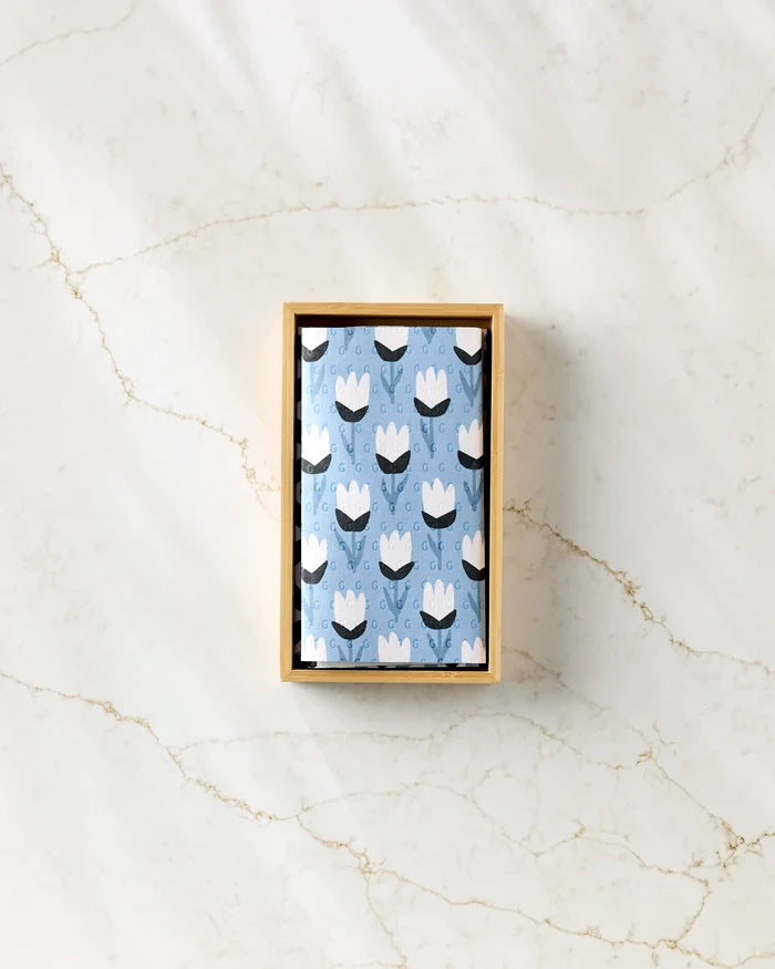 Forest Findings by Anette Heiberg: a wooden box holds a folded blue cloth with a white and black tulip pattern, resembling reusable paper towels, displayed on a light marbled surface.