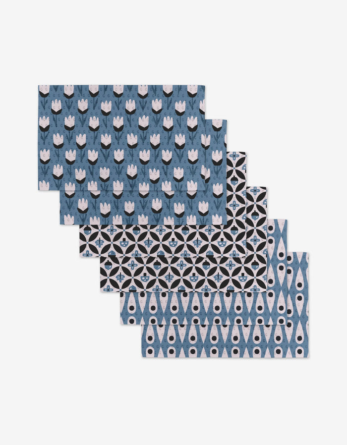 Five Forest Findings rectangular placemats by Anette Heiberg, featuring blue, black, and white geometric and floral patterns, are stacked on a white background—an eco-friendly alternative to paper towels.