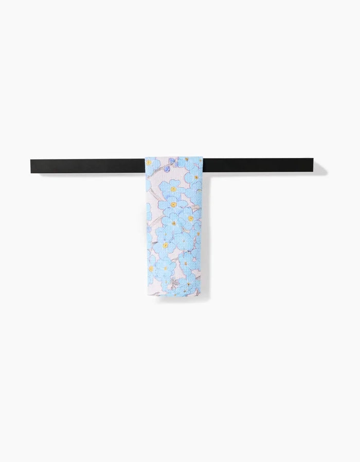 The Pascale Dilger Forget Me Not Floral light blue scarf, crafted from recycled materials and featuring a floral design, is draped neatly over a sleek black rod against a plain white background.