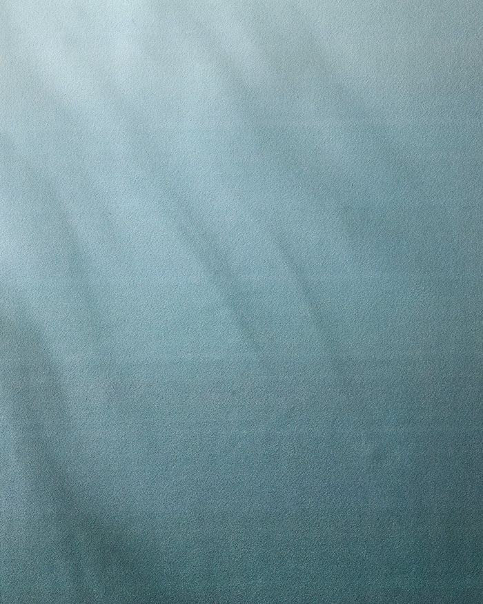 A textured blue surface with soft light and shadow gradients evokes the feel of the GEOMETRY Foundation yoga towel, with faint lines suggesting gentle movement or subtle patterns across the design.