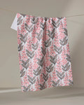 The Foxglove Finery kitchen towel by Sarah Daugherty features a pink and black botanical leaf and berry pattern on white eco-friendly fabric, hanging on a clothesline with a neutral backdrop.