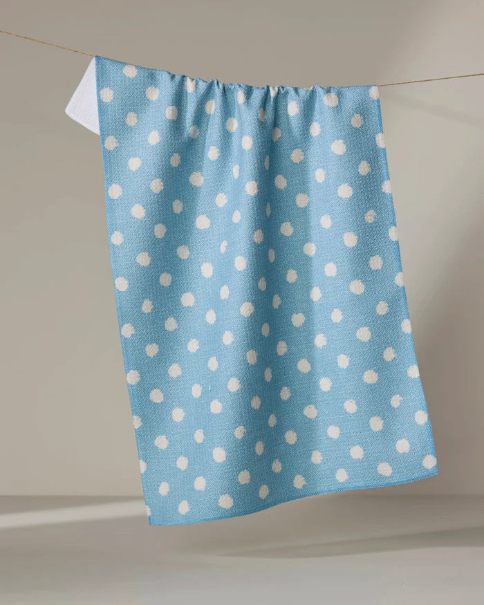The Geometry Freckle Light Blue tea towel, made from recycled materials and featuring white polka dots, hangs on a clothesline against a simple light background.