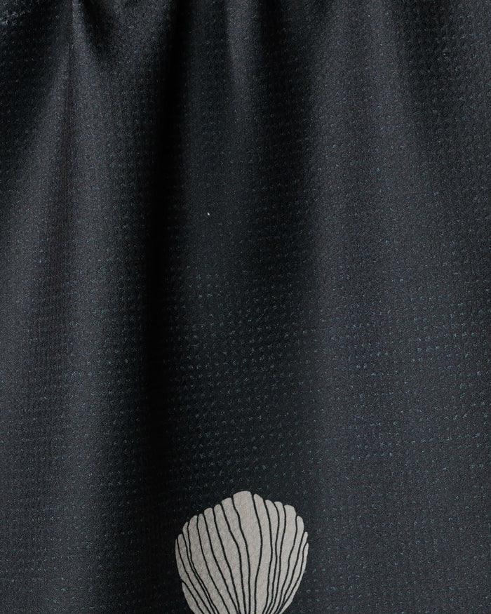 A close-up of Freja by Anna Christian shows dark recycled fabric with a subtle dotted texture and a single white seashell design near the bottom center.