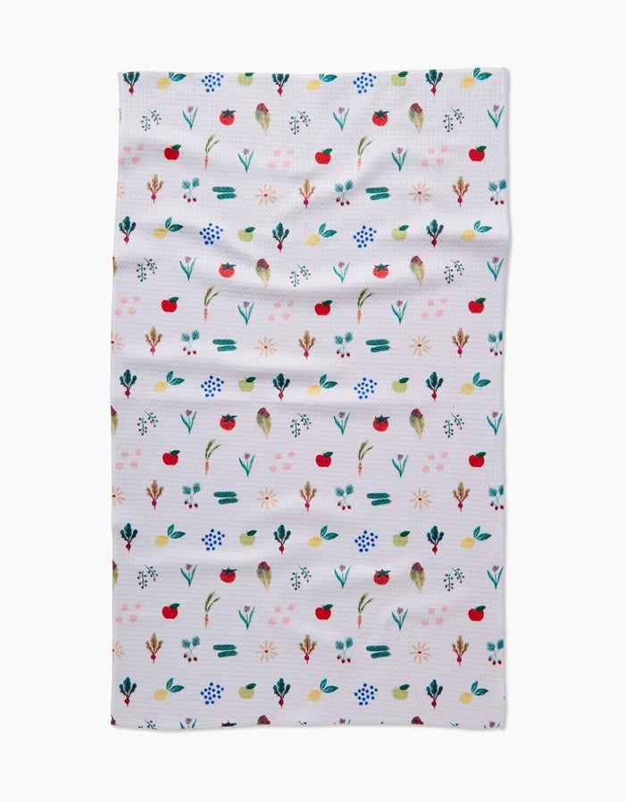 The Brittany Jepsen Fresh Produce tea towel features small, colorful red, blue, green, and yellow flowers and leaves arranged in neat rows on white fabric with a slightly wrinkled texture.