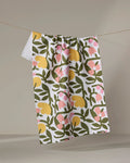 The Fresh Vines tea towel by Lisa Nelson features a colorful green, yellow, and pink floral pattern on white Geoweave fabric. It hangs on a beige string against a neutral background, perfect for everyday use.