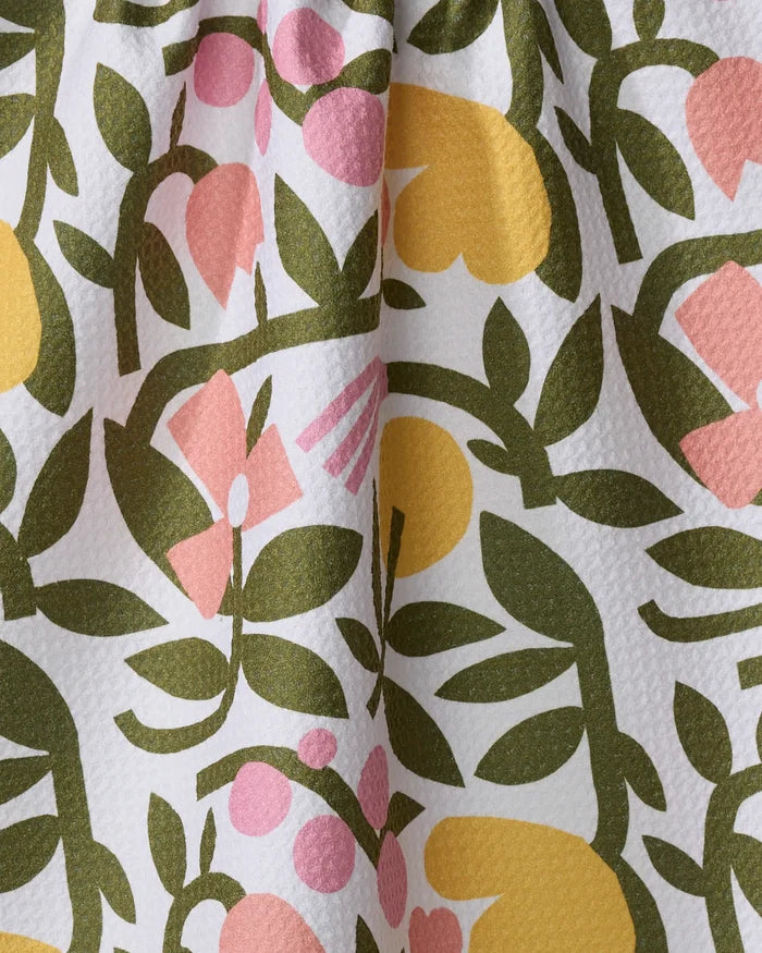 A close-up of Lisa Nelson's Fresh Vines tea towel shows textured Geoweave fabric made from recycled materials, featuring a colorful floral pattern with green leaves, yellow shapes, and pink flowers on a white background.