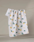 The "Freshly Picked" tea towel by Sara Mari, featuring a yellow lemon and green leaf pattern on white textured recycled fabric, hangs on a string against a light background.