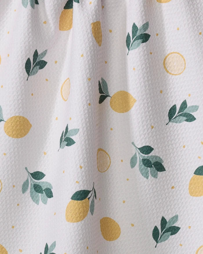 The Sara Mari "Freshly Picked" tea towel features a white textured fabric with yellow lemons, lemon slices, small yellow dots, and green branches. Made from quick-drying recycled materials for everyday convenience.