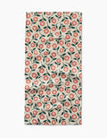 A slightly wrinkled Megan Kampa Friendly Floral Peach Geoweave bar towel, with a repeating red and pink flower and green leaf pattern on cream, is displayed on a white surface.