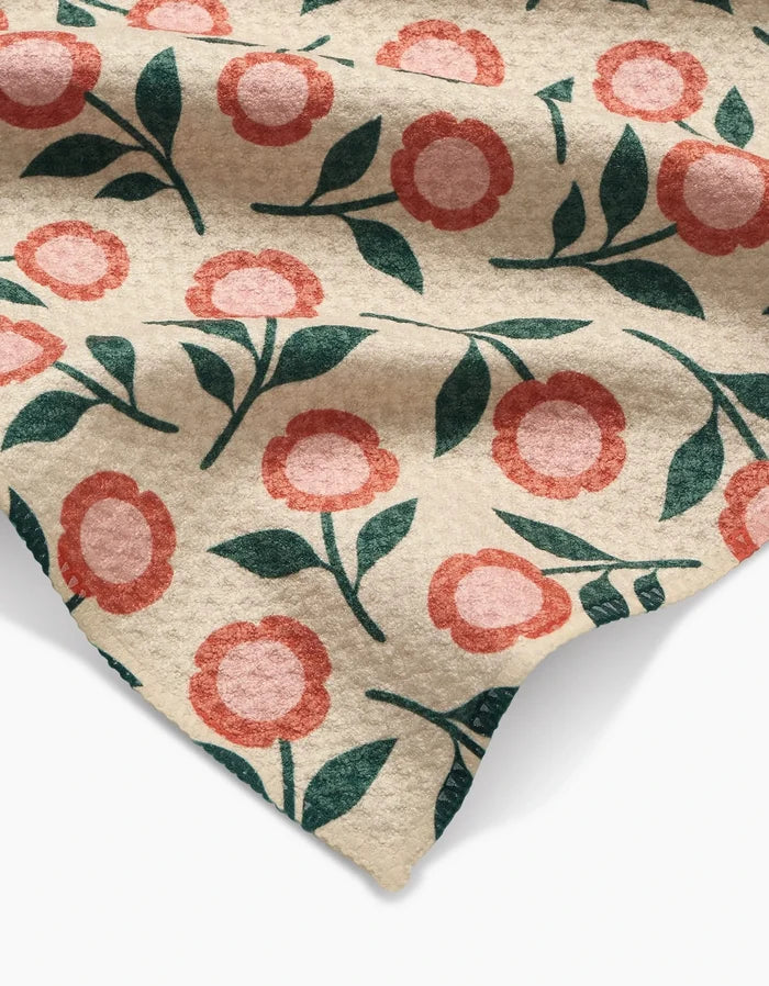 Friendly Floral Peach by Megan Kampa features beige Geoweave fabric with a repeating pattern of simple red and pink flowers and green leaves, shown draped in soft folds and shadows.