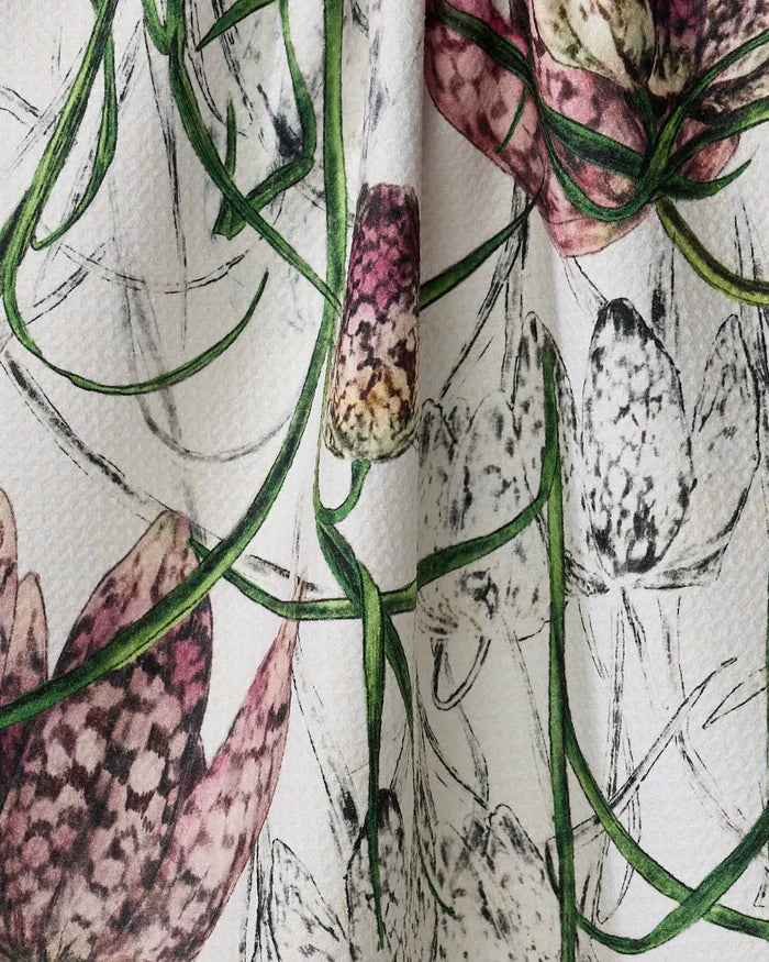 A close-up of Pascale Dilger’s Fritillaria recycled kitchen towel, showing textured fabric with pink, green, and white checkered flowers and green vines on a white background.