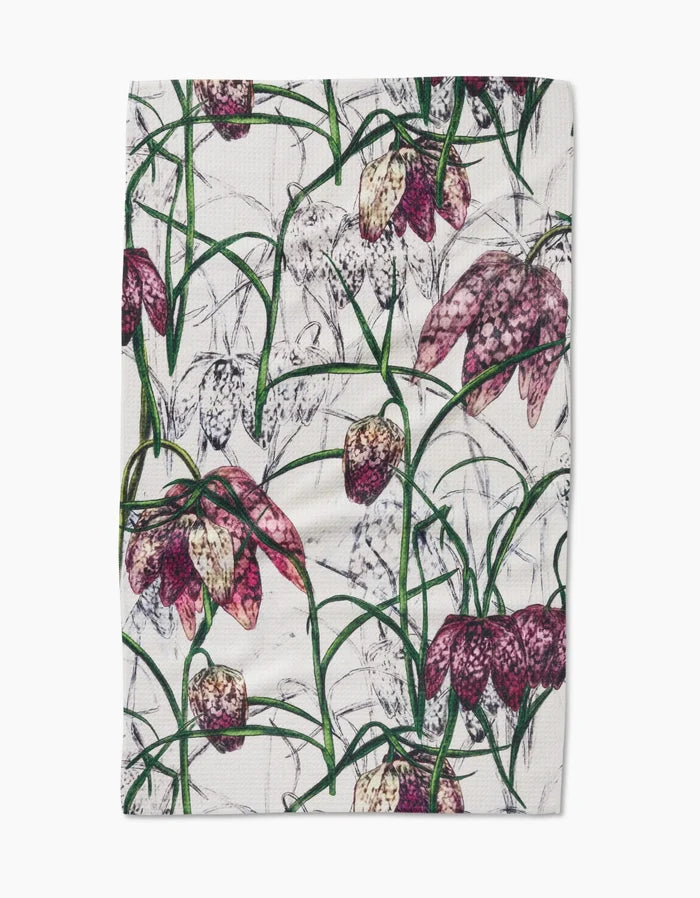 The Fritillaria tea towel by Pascale Dilger features a rectangular design with purple, white, and pink checkered flowers and green stems on a crisp white Geoweave fabric.