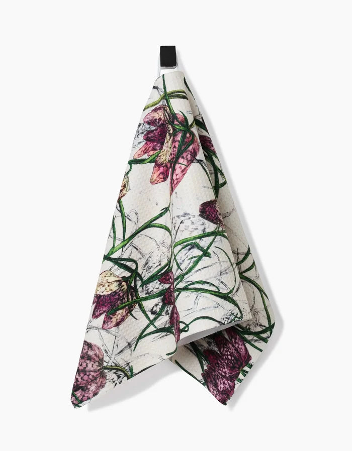 The Pascale Dilger Fritillaria bar towel features a botanical print of purple and pink flowers with green leaves on ultra-absorbent white Geoweave fabric, and hangs from a black loop.