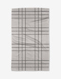 The Becki Owens Frosty tea towel features a light gray color with a simple black grid pattern, crafted from ultra-absorbent recycled materials, and is shown flat on a white background.