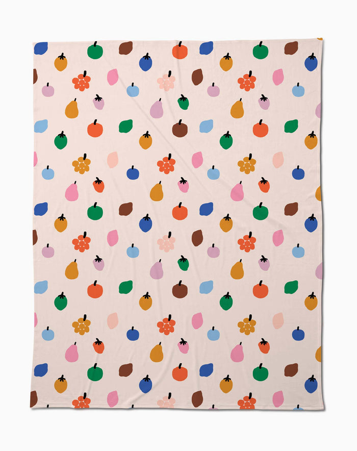 The Fruit Basket Butter Blanket by Jennifer Bouron is a beige, eco-friendly throw made from recycled materials, featuring a playful mix of fruit shapes, blobs, and flowers in vibrant colors.