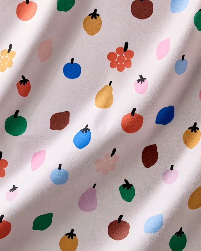 The Fruit Basket dinner napkin set by Jennifer Bouron features colorful, stylized fruit shapes in red, green, blue, yellow, pink, and orange on an absorbent wavy-textured fabric for a cheerful, whimsical look.