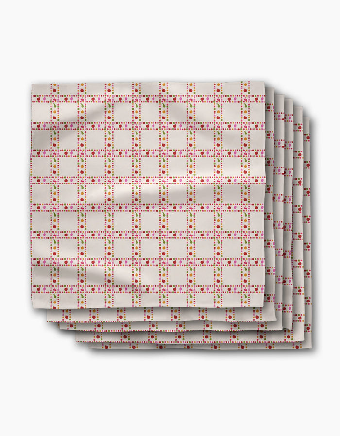 Four folded Fruits Plaid napkins by Geometry, made from Geosuede fabric, feature a grid of pink and red squares with yellow outlines on a light beige background, displayed on a white surface.