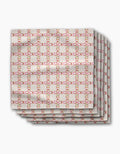 Four folded Fruits Plaid napkins by Geometry, made from Geosuede fabric, feature a grid of pink and red squares with yellow outlines on a light beige background, displayed on a white surface.