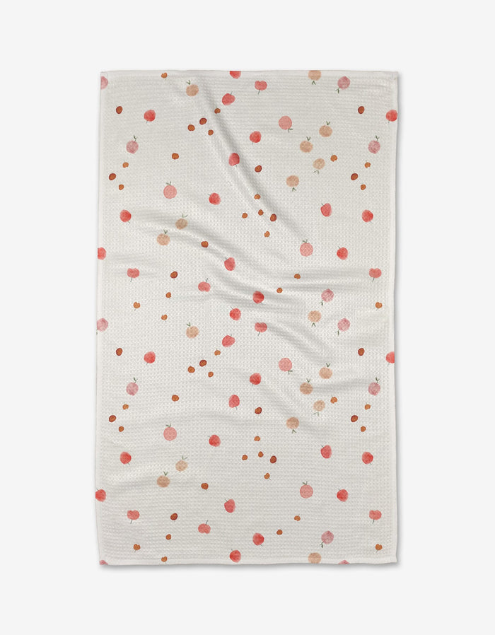 The Fruity blanket by Anee Shah is a white, textured throw with small pink and orange pomegranate illustrations and brown dots, resembling an ultra-absorbent towel. It’s shown laid flat with gentle wrinkles.