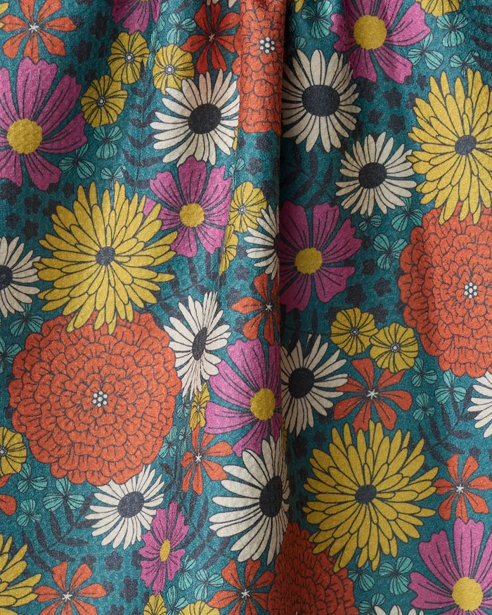A close-up of Megan Kampa’s Funky Fleurs recycled kitchen towel, showcasing vibrant yellow, orange, white, and pink flowers with green leaves on a teal background. The dense retro-inspired design brings charm to this eco-friendly tea towel.