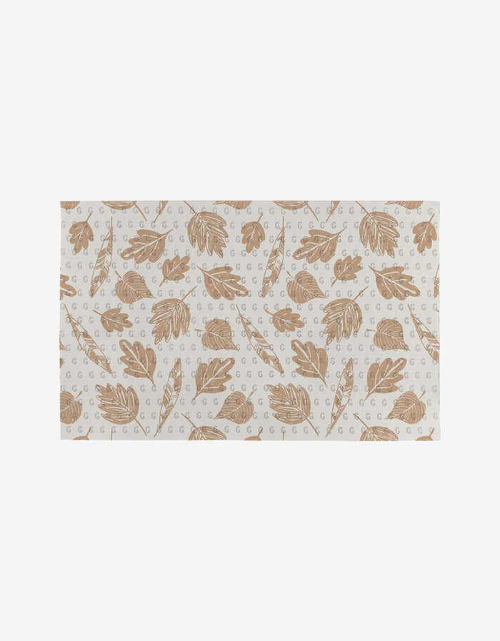 Garden Bloom by Hufton Studio is a rectangular mat featuring a repeating pattern of light brown leaves and branches on white, accented with small gray G letters. Made from post-consumer recycled materials.