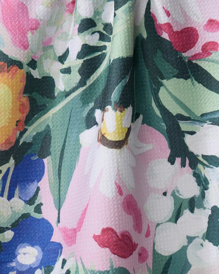 A close-up of Ania Zwara Art's "Garden Bouquet" tea towel shows its ultra-absorbent, dimpled fabric with a colorful floral print featuring pink, white, yellow, green, and blue flowers and leaves.