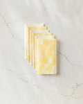 A stack of six folded GEOMETRY Garden of Gold yellow reusable paper towels with a white floral pattern, displayed on a white marble surface with subtle veining.