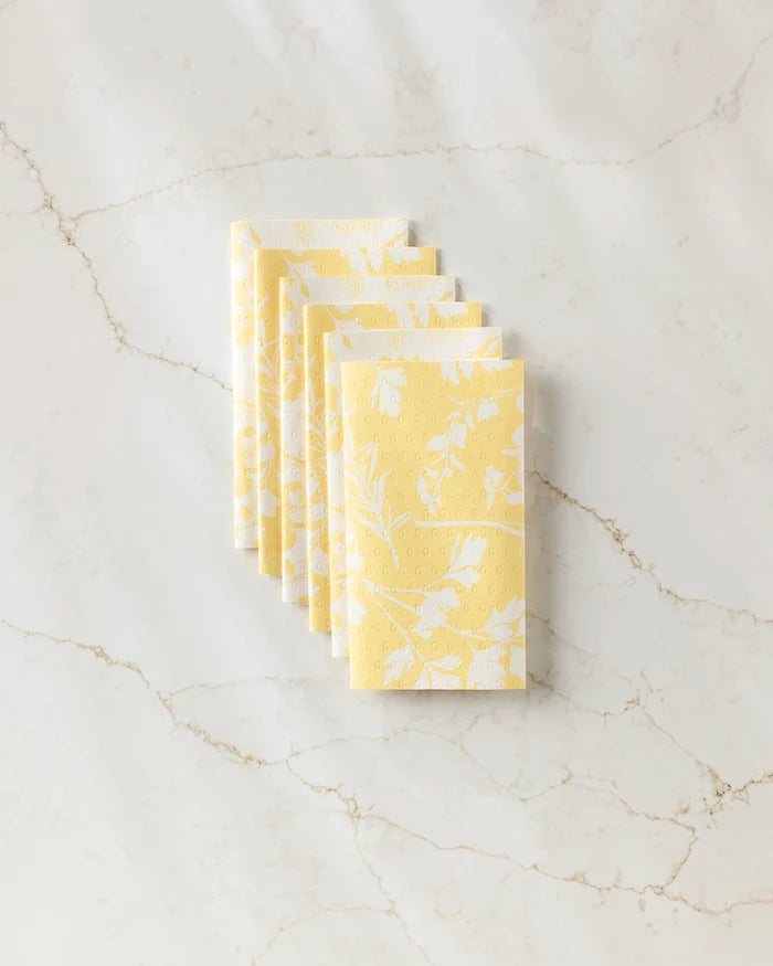 A stack of six folded GEOMETRY Garden of Gold yellow reusable paper towels with a white floral pattern, displayed on a white marble surface with subtle veining.