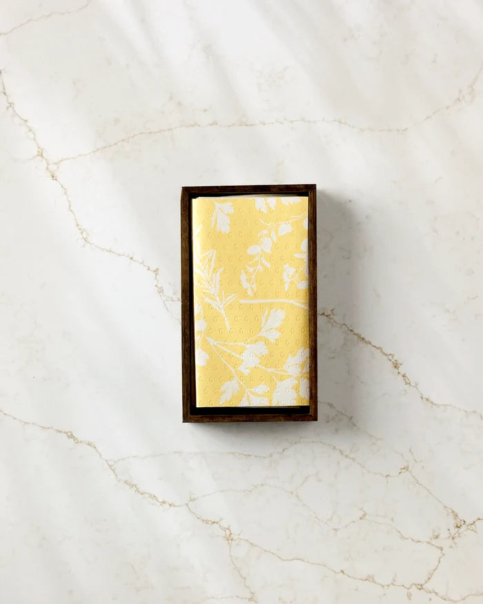 The GEOMETRY Garden of Gold soap features a yellow bar with a white botanical pattern, displayed in a dark wood tray on marble and paired with reusable paper towels for an eco-friendly, stylish accent.