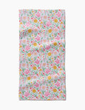 The Garden of Light bar towel by Danelys Sidron features a colorful floral pattern—pink, yellow, and orange flowers with green leaves—on white Geoweave fabric made from recycled materials. The material has a slightly wrinkled look.