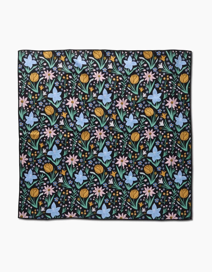 The Garden of Light by Danelys Sidron is a square fabric with a black background and a repeating pattern of colorful yellow, pink, and blue flowers with green leaves, made from highly absorbent post-consumer recycled materials.