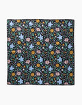 The Garden of Light by Danelys Sidron is a square fabric with a black background and a repeating pattern of colorful yellow, pink, and blue flowers with green leaves, made from highly absorbent post-consumer recycled materials.