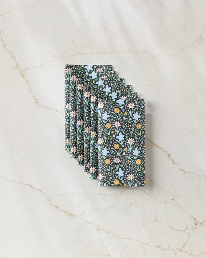 Six “Garden of Light” reusable paper towels by Danelys Sidron, featuring a blue, yellow, and white floral pattern, are neatly fanned out on a white marble surface with light brown veining.