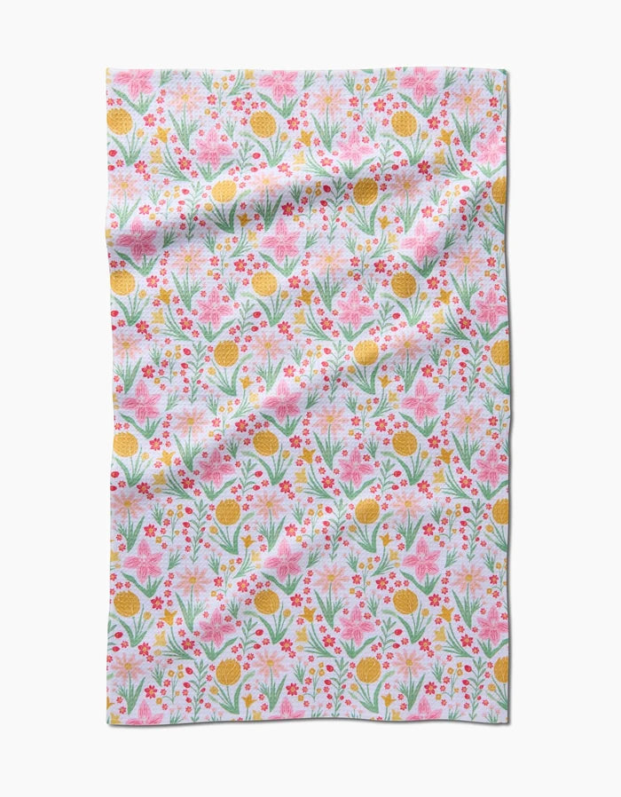 Danelys Sidron’s “Garden of Light” is a rectangular cloth made from recycled materials, featuring pink, yellow, and red flowers with green leaves on a white background. The slightly wrinkled fabric shows off its colorful floral pattern.
