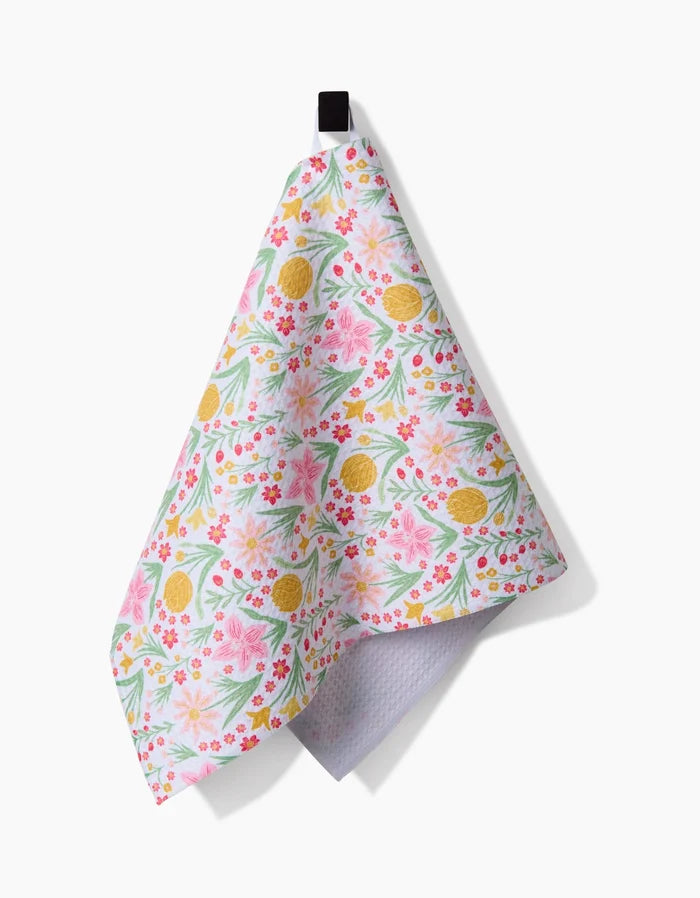 The Danelys Sidron Garden of Light bar towel, featuring a pink, green, and yellow floral and lemon pattern, hangs from a black loop against a white background. Crafted with Geoweave fabric for superior absorbency.