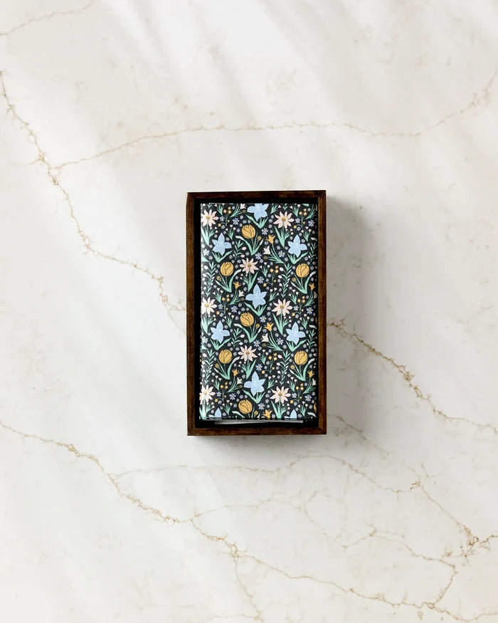 The Danelys Sidron “Garden of Light” rectangular soap bar features a blue, white, and yellow floral pattern and sits in a wooden tray on marble, paired with eco-friendly paper towels for a sustainable touch.
