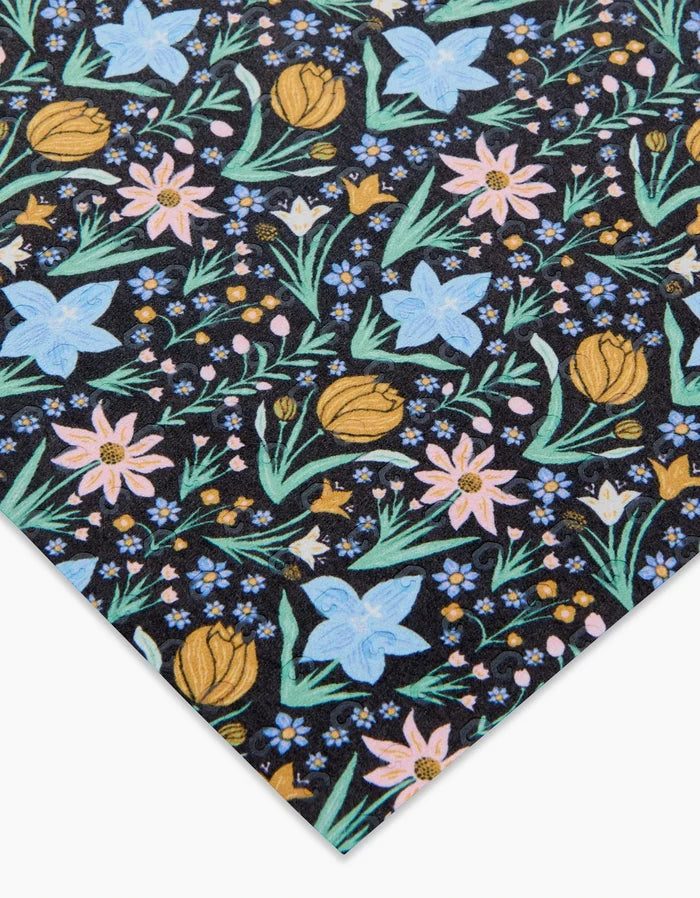 The Danelys Sidron Garden of Light sheet features blue, pink, and yellow floral patterns with green leaves on black post-consumer recycled paper, viewed at an angle to show a partial design.