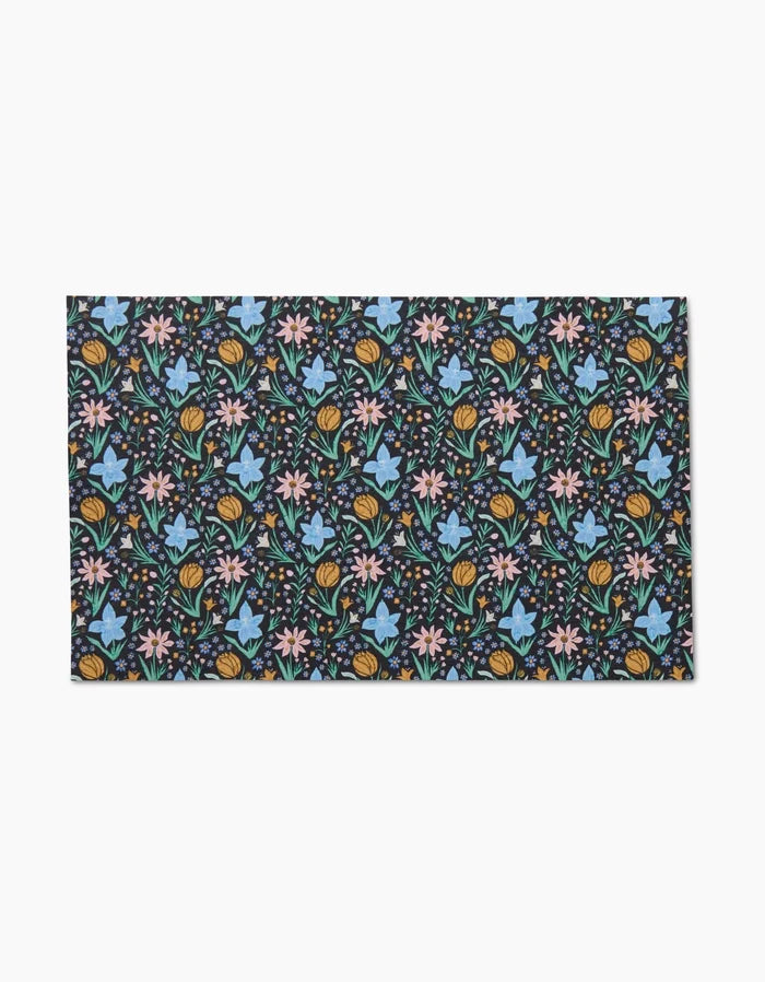 The Garden of Light mat by Danelys Sidron features a dark background with blue, pink, and yellow flowers and green leaves. Made from eco-friendly post-consumer recycled materials, this rectangular mat brightens any space with its vibrant floral design.