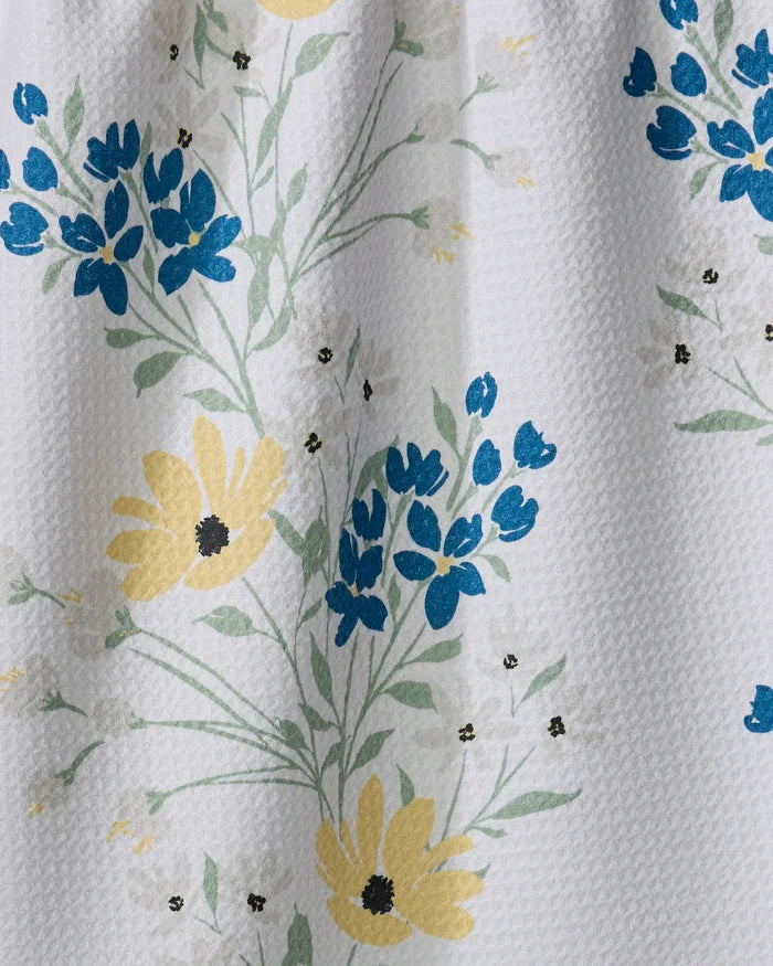 The "Garden Picks" dish towel by Ashley Celena features a white textured fabric with yellow and blue floral clusters and green stems, creating a fresh, delicate pattern—perfect for adding brightness to your kitchen.