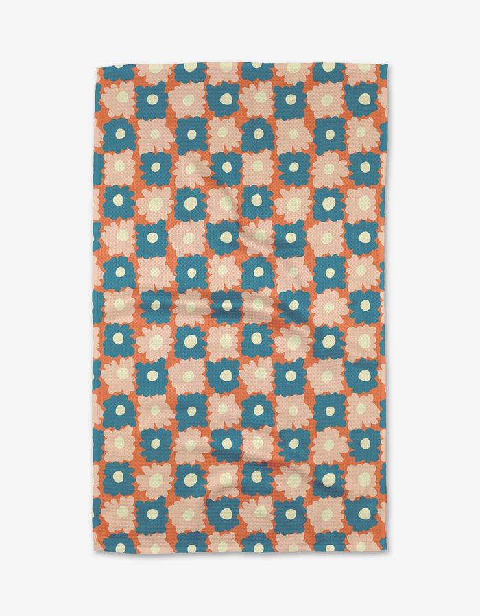 The Garden Plot tea towel by Kelsey Weigl features blue and cream flowers in a geometric grid on an orange background, printed on soft Geoweave™ fabric.