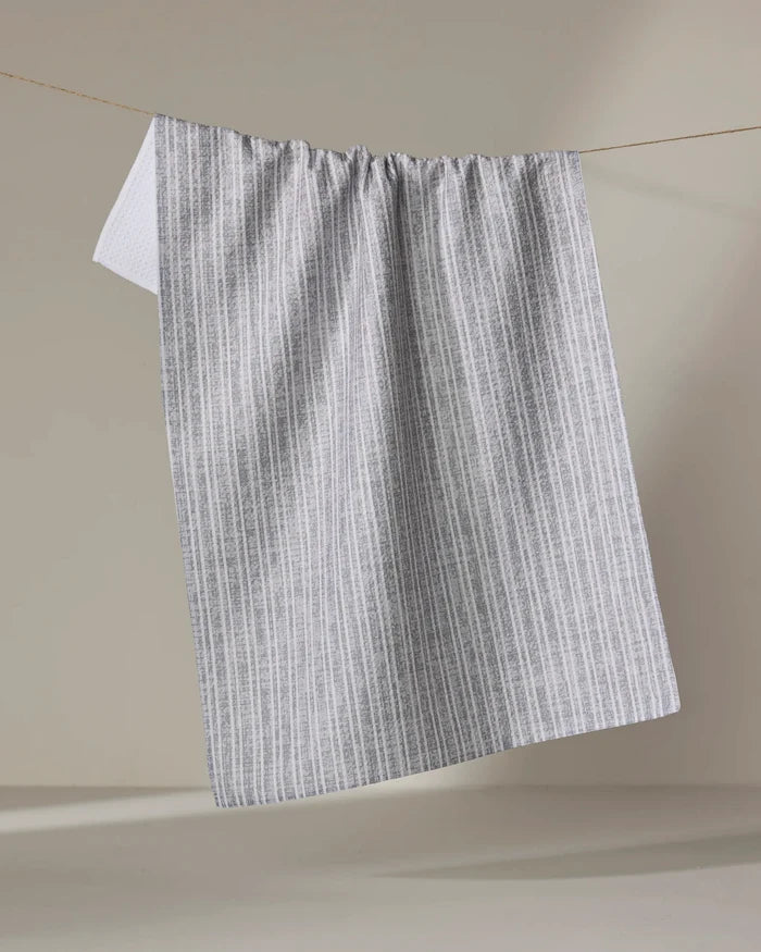 The Becki Owens Garff Grey towel, featuring thin vertical gray stripes on white, hangs on a clothesline against a light background.