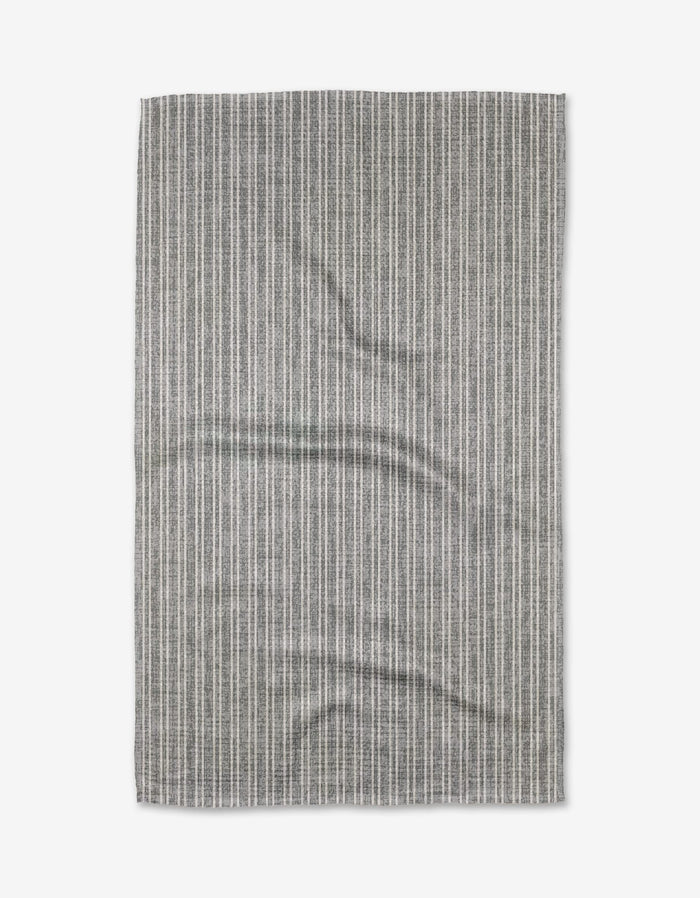 A rectangular Garff Grey tea towel by Becki Owens, featuring thin vertical white stripes and a slightly wrinkled texture, is laid flat on a white background.