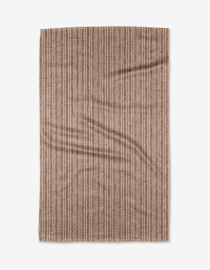 The Garff Rust by Becki Owens is a rectangular Geoweave fabric with a brown background and vertical white dashed stripes, shown laid flat with slight wrinkles on a plain white surface.