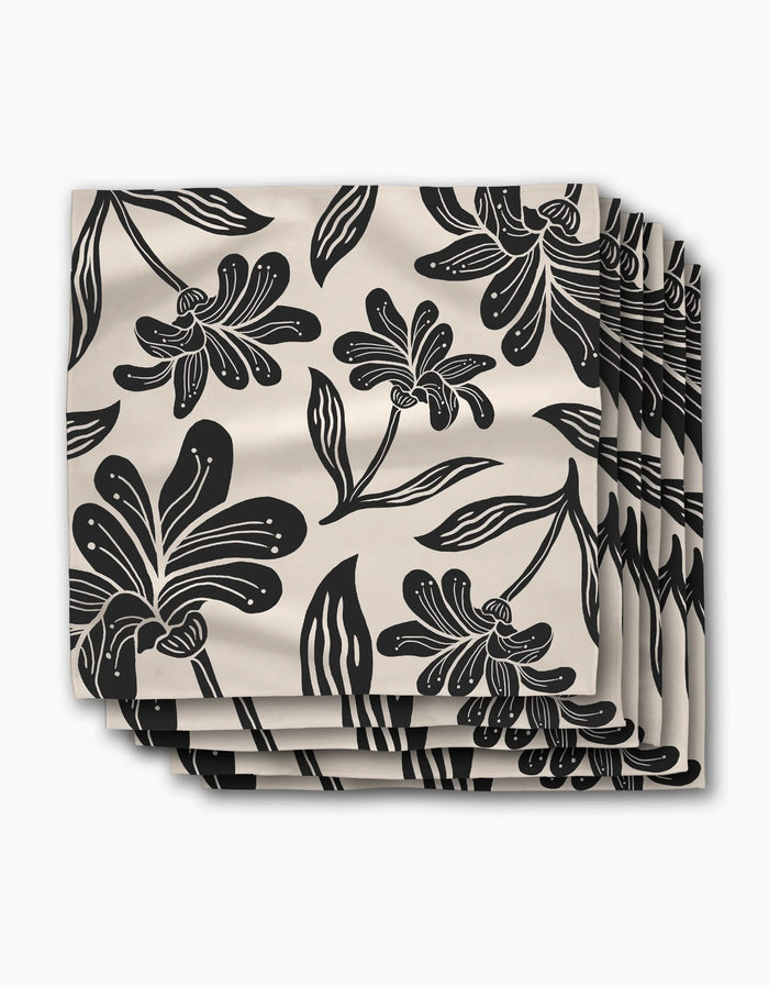 A set of four beige Geometry napkins in the Giant Lush Floral pattern, featuring bold black flowers and leaves, stacked and slightly fanned against a white background.