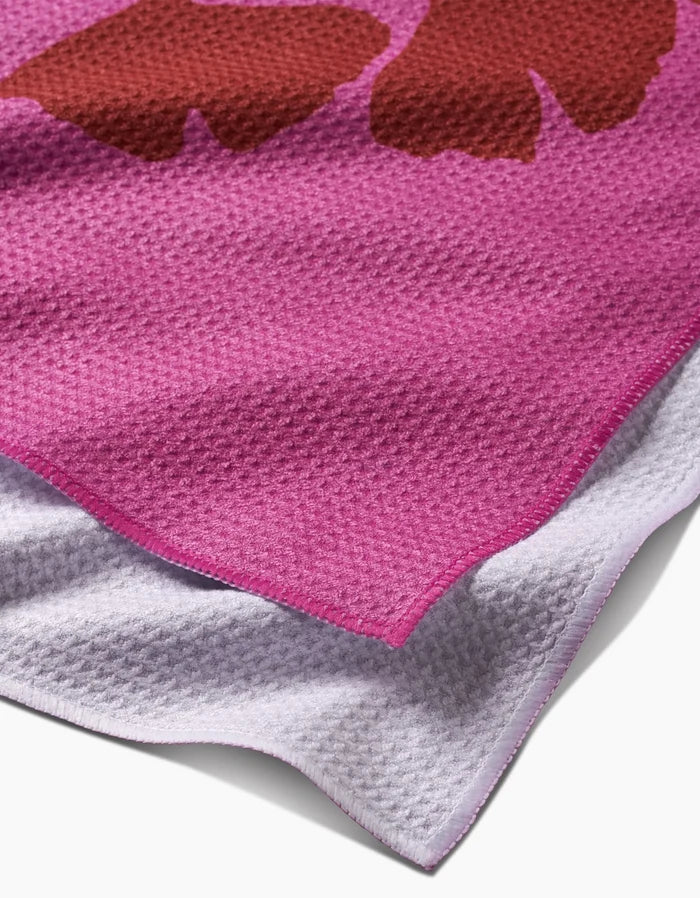 A close-up of PrintedPlant’s Ginkgo towel shows its pink and purple Geoweave fabric with a brown abstract shape and a neat pink border, highlighting the ultra-absorbent edge.