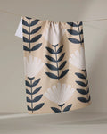 The Gloria kitchen tea towel by Amy MacCready, crafted from recycled materials, displays large black and white stylized flowers and leaves on beige fabric, hanging on a clothesline against a neutral backdrop.