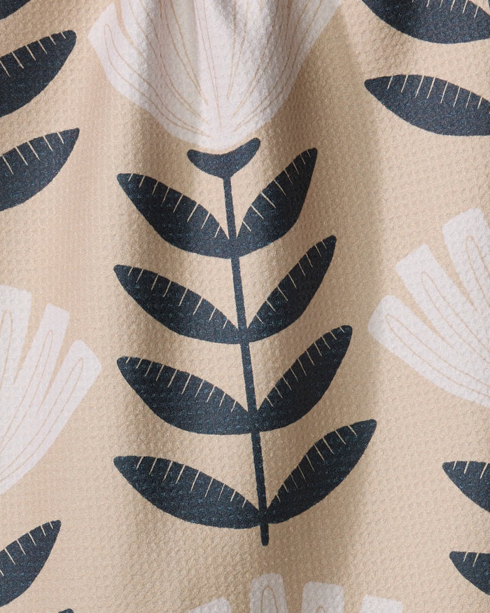 Gloria by Amy MacCready is a modern, minimalistic kitchen tea towel made from recycled materials. It features a beige background with black stylized leafy branches and white geometric flowers for an eco-friendly touch.